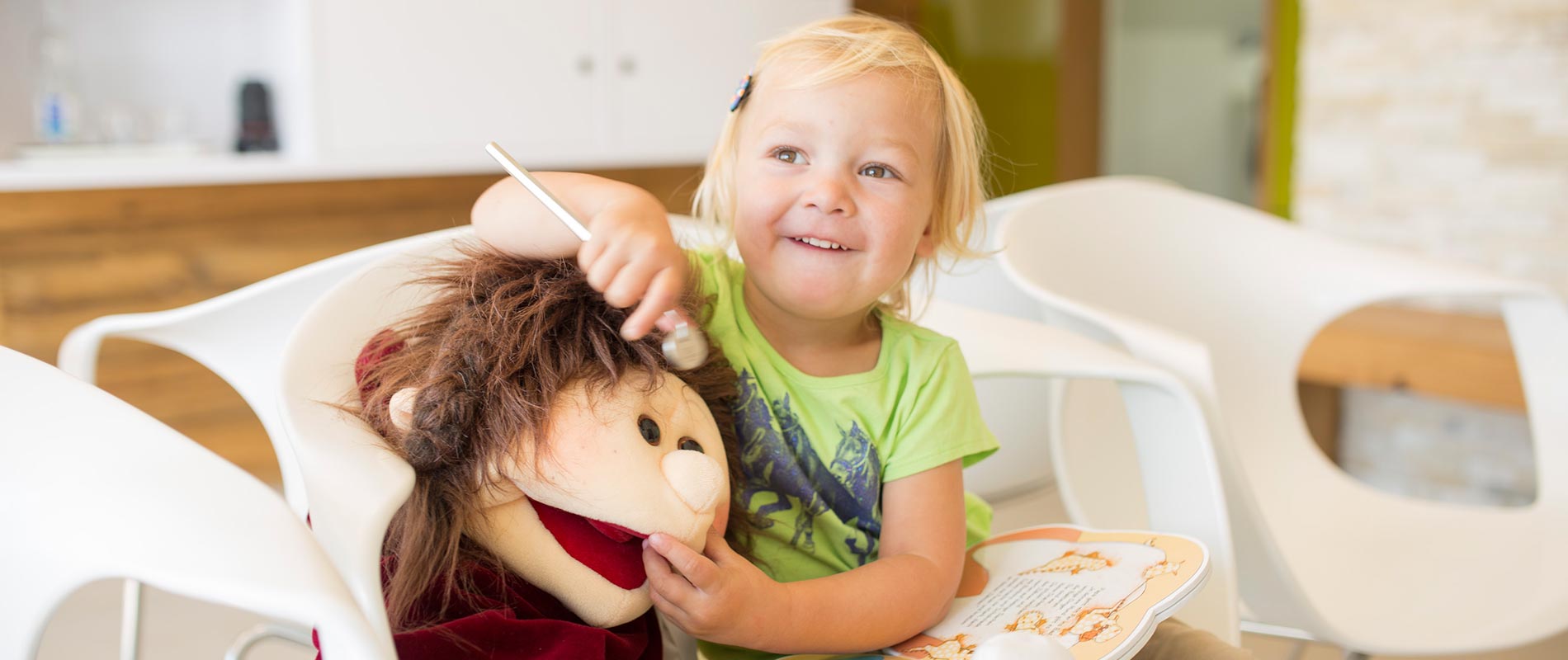 Kind spielt Zahnarzt mit Stoffpuppe im Wartezimmer der Zahnarztpraxis.