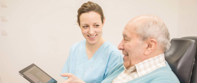 Zahnärztin erklärt älterem Patienten Behandlungsplan auf Tablet.