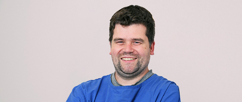 Zahnarzt in blauer Uniform lächelt in die Kamera.