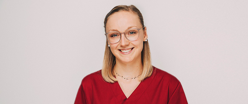 Freundliche Zahnärztin in roter Arbeitskleidung lächelt in die Kamera.